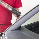 Glazier using application gun to apply adhesive for windscreen